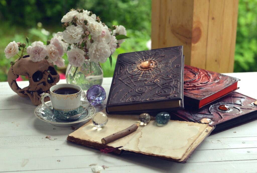Vintage summer still life with old spell book, diary, cup, roses and magic objects.